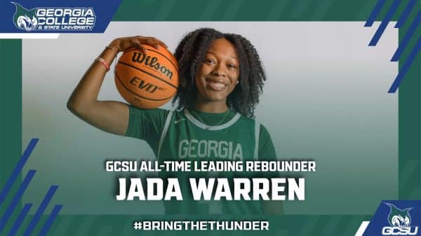 Black female college basketball player, Jada Warren, wearing a green jersey, holding a basketball on her shoulder and smiling at the camera.