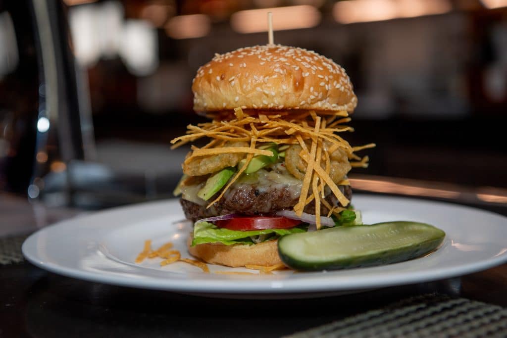 A large burger on a plate next to a pickle