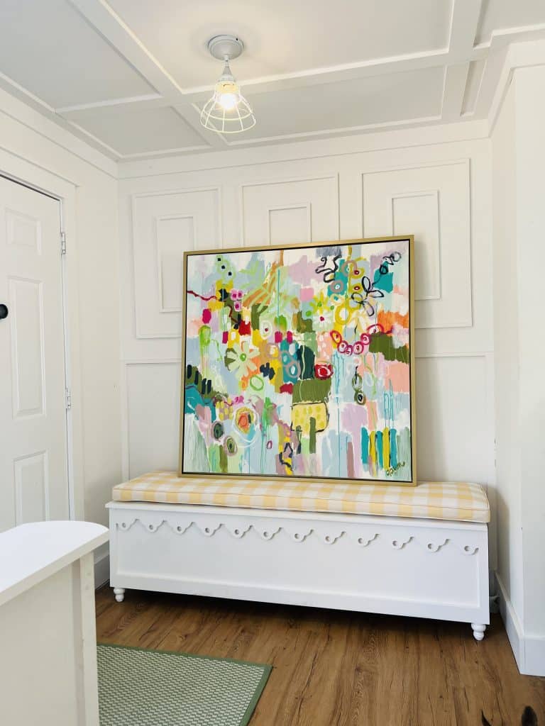 Colorful, mixed-media painting that's framed and sitting on a white and cream-colored piece of furniture against a white wall