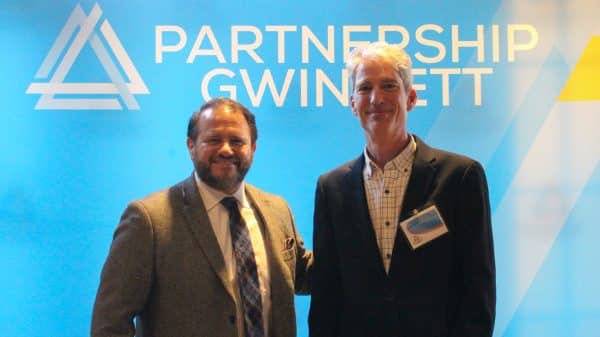 Two men in suits smiling and standing next to each other in front of Partnership Gwinnett backdrop with white lettering on blue background.