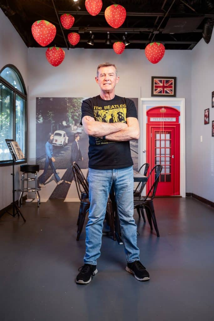 A man wearing a Beatles t-shirt standing in a cafe that has Beatles memorabilia