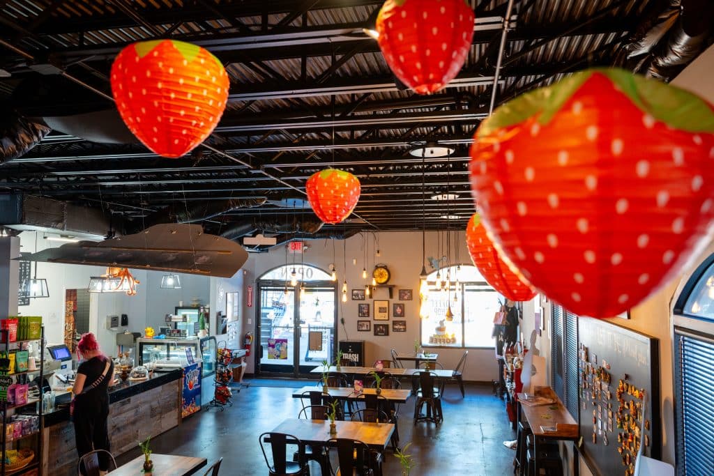 Cafe interior with dark floors, a row of tables and counter. There are large strawberry decorations hanging from the ceiling