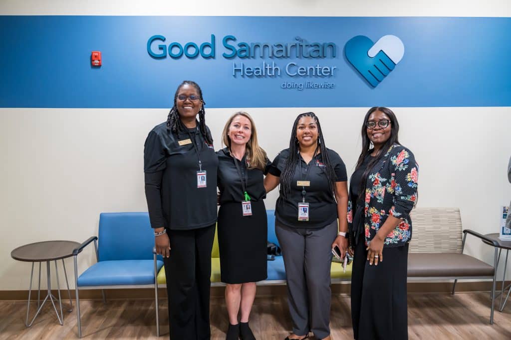 Four women standing in front of a blue and white wall with the Good Samaritan Health Center name and logo.