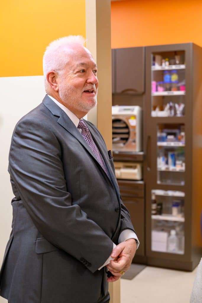 An older white man with white hair, wearing a suit and standing in the hallway of a new healthcare center