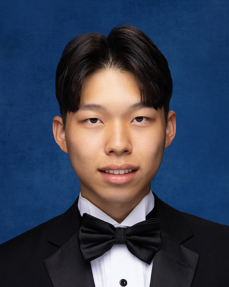 High School senior photo of a young Asian man with short hair, parted in the middle. He's wearing a tux with bowtie and white shirt and smiling.
