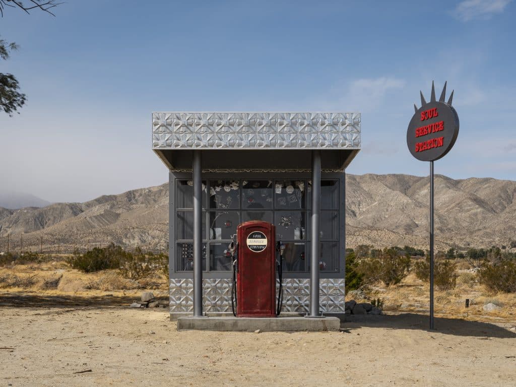 Mixed media installation, Soul Service Station, by Alison Saar. It looks an old single-pump service station building with sign, set outdoors in the desert at Coachella.
