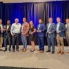A group of eight men and one woman standing on stage with business awards they received from Partnership Gwinnett in April 2025.