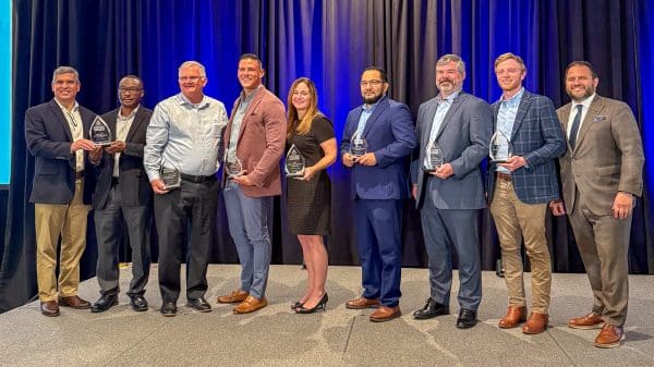 A group of eight men and one woman standing on stage with business awards they received from Partnership Gwinnett in April 2025.