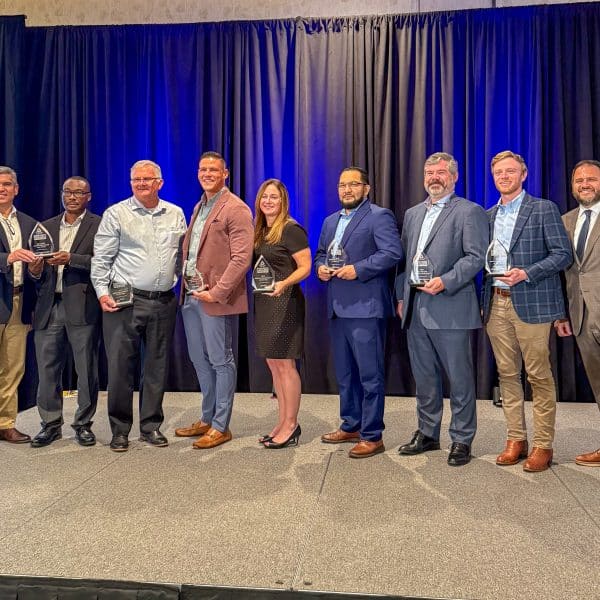 A group of eight men and one woman standing on stage with business awards they received from Partnership Gwinnett in April 2025.
