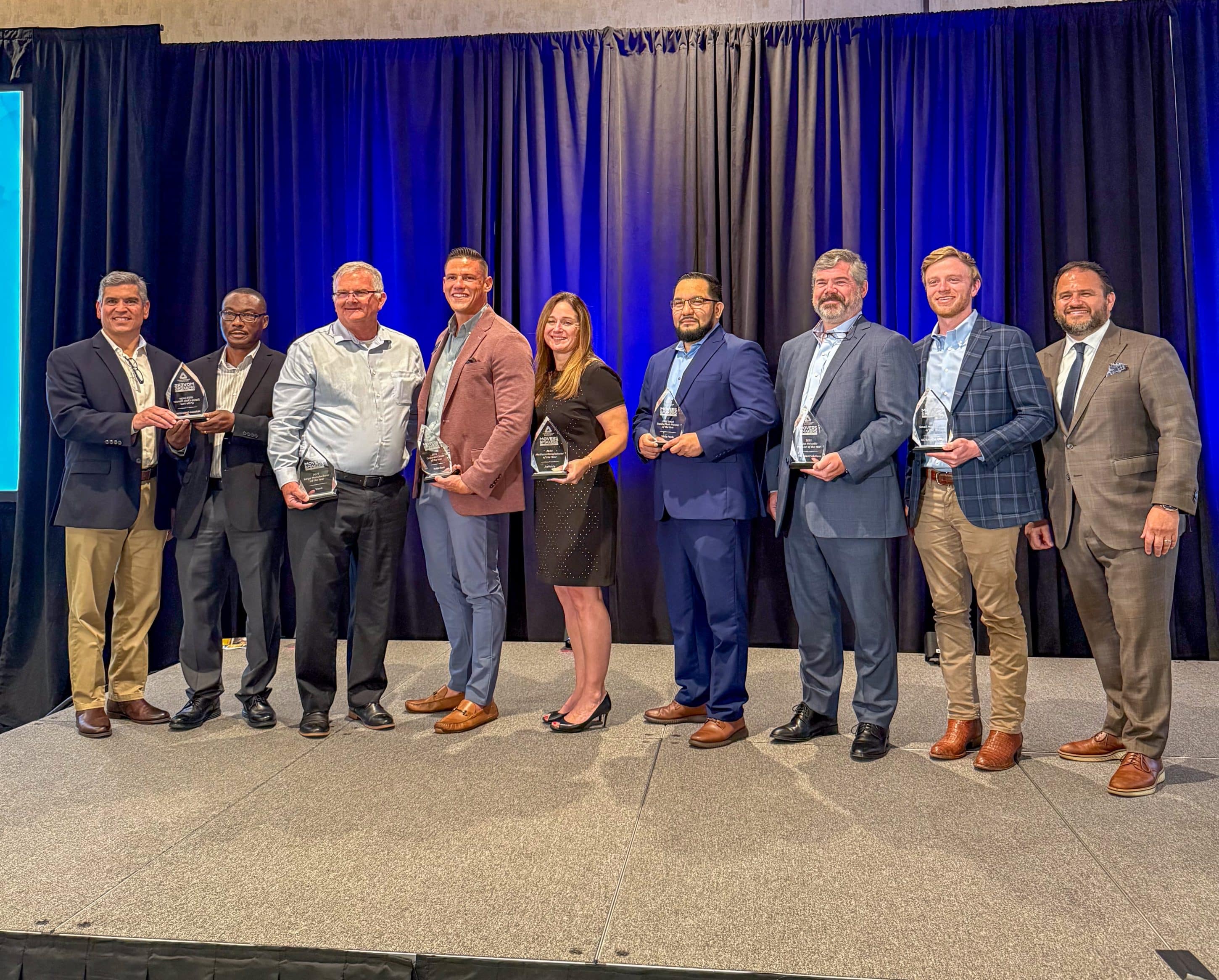 A group of eight men and one woman standing on stage with business awards they received from Partnership Gwinnett in April 2025.