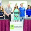 A group of people standing behind a table and podium at a business event where they will be speaking.