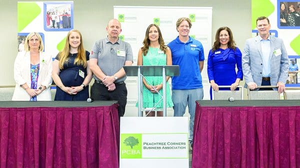 A group of people standing behind a table and podium at a business event where they will be speaking.