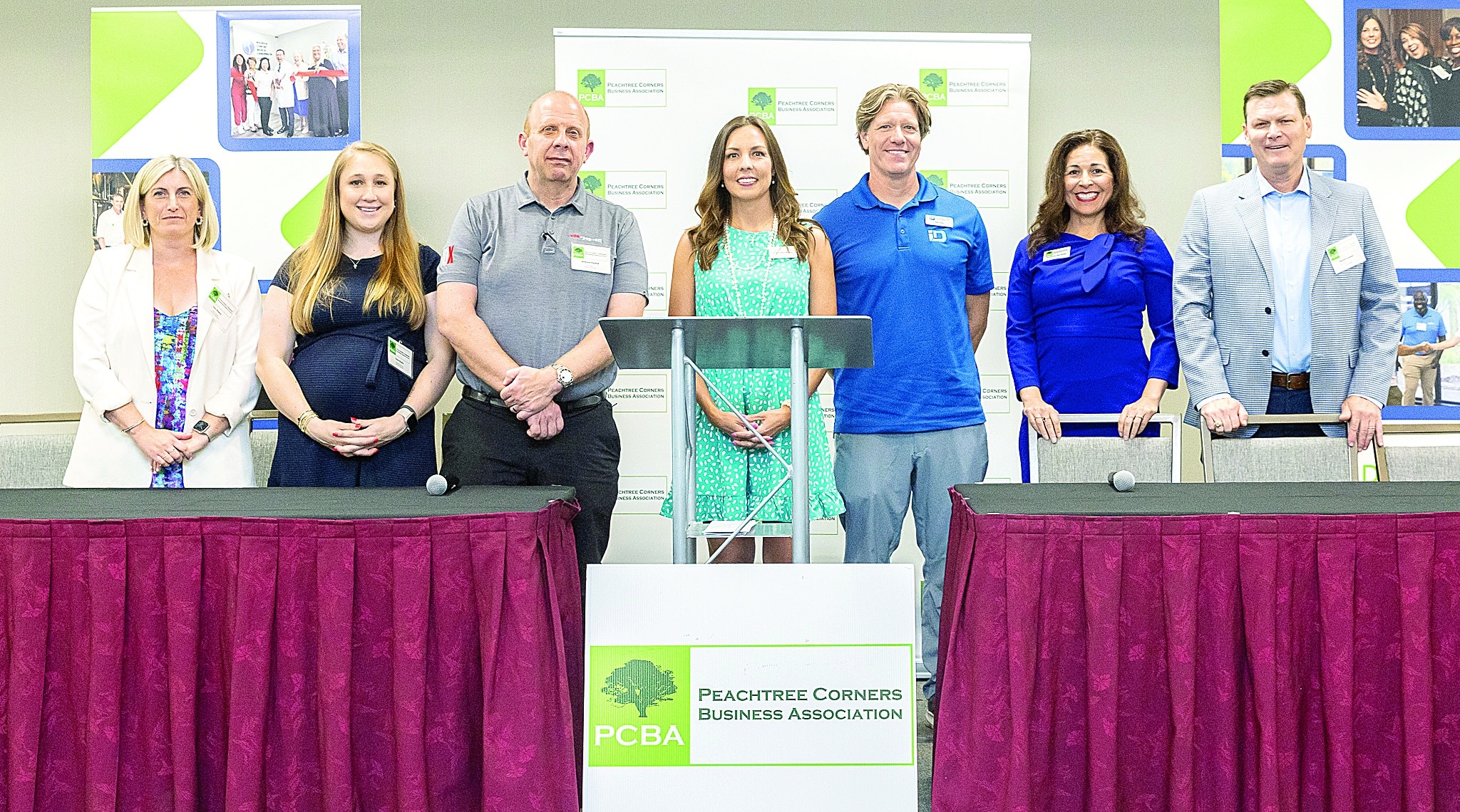 A group of people standing behind a table and podium at a business event where they will be speaking.