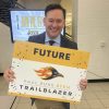 A man holding a Paul Duke STEM High School Trailblazers sign and smiling at the camera.